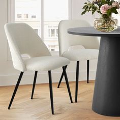 two white chairs sitting at a round table with flowers in vase on top of it