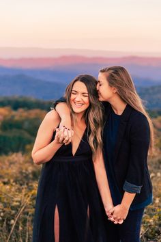 two women standing next to each other on top of a hill with mountains in the background