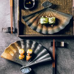 an assortment of sushi and chopsticks on a tray next to a fan