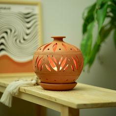 an orange vase sitting on top of a wooden table next to a potted plant