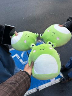 three green stuffed animals sitting on top of each other in front of a person's hand