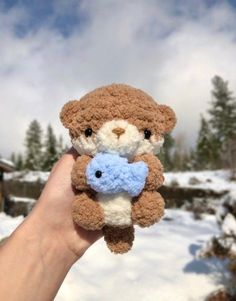 a hand holding a small teddy bear in the snow