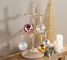 a christmas tree with ornaments and candles on a wooden table in front of a wall