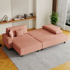 a pink couch sitting on top of a wooden floor next to a window in a living room