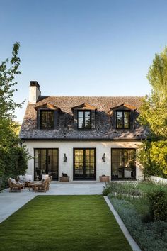 a white house with black shutters and windows on the roof is surrounded by greenery