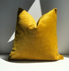 a yellow pillow sitting on top of a white table next to a shadow cast wall