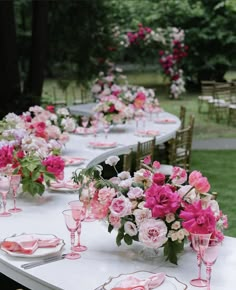 a long table with pink and white flowers in vases, plates and napkins