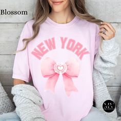 Boho Pink Bow Coquette New York Shirt Gift for Her Aesthetic Cherries Tee NYC Shirt Summer Cottagecore Tshirt Gardening Gift Trendy Crewneck Capture the vibrant energy of the Big Apple with our New York Boho Pink Bow Shirt, featuring a bold and playful twist on the iconic cityscape. Crafted on a Comfort Colors trendy crewneck, this eye-catching design showcases a cute luxury style pink coquette bow, offering the urban chic charm of New York City. Perfect for New York enthusiasts, and anyone with Cute Pink Shirt With Text Print, Spring Pink Slogan Shirt, Pink Slogan Shirt For Spring, Spring Kawaii Shirt With Graphic Print, Spring Kawaii Letter Print Tops, Cute Text Print Shirt For Spring, Kawaii Crew Neck Shirt With Letter Print, Cute Crew Neck Shirt With Text Print, Spring Pink Shirt With Text Print