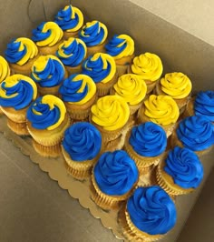 cupcakes with blue and yellow frosting are in a box on the table