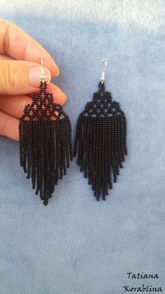 a pair of black beaded earrings with tassels hanging from the ends, on a blue background