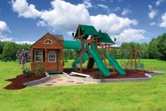 a wooden play structure with a green slide in the middle of it and grass on the ground