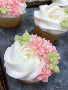 three cupcakes with white frosting and pink flowers on them sitting on a tray