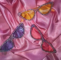 three pairs of colorful sunglasses laying on pink satin