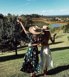 two women standing on top of a lush green field holding wine glasses in their hands