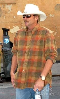 a man in a cowboy hat and sunglasses walking down the street with his skateboard