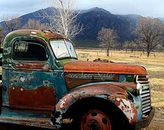 an old rusted out truck sitting in a field