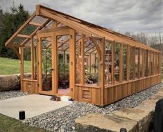 a small wooden greenhouse sitting on top of a gravel field next to a tree stump