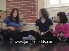 three women are sitting on the floor playing guitar together, and one woman is singing