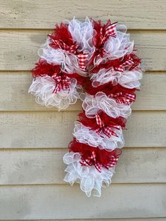 a red and white mesh wreath hanging on the side of a wooden wall with burlocks