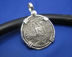 an old silver coin sitting on top of a black leather cord with a blue background