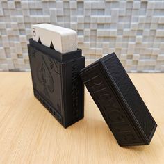 two black and white business card holders sitting on a wooden table in front of a tiled wall