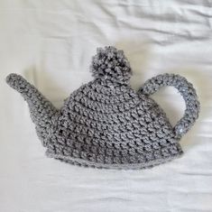 a crocheted gray tea pot sitting on top of a white bed covered in blankets