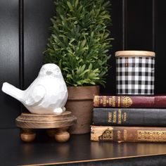 a white bird statue sitting on top of a wooden table next to books and a potted plant