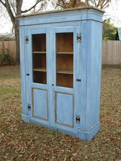 an old blue cabinet is sitting in the grass with leaves on the ground around it