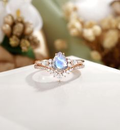 a white diamond ring sitting on top of a table with flowers in the back ground