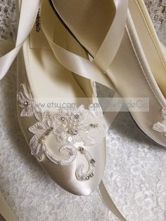 white wedding shoes with flowers and pearls on the heel are sitting on a lace covered surface