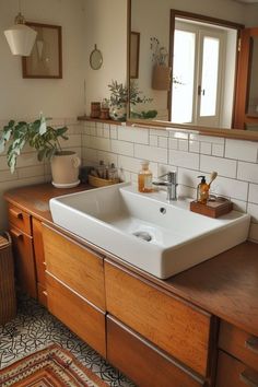 a white sink sitting on top of a wooden counter next to a mirror and potted plant