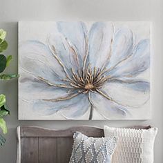 a large white flower is hanging on the wall above a bed with pillows and throw pillows