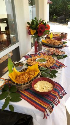 a table full of food and drinks on the outside patio with flowers in vases