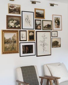 there are many framed pictures on the wall above two chairs and one chair is upholstered