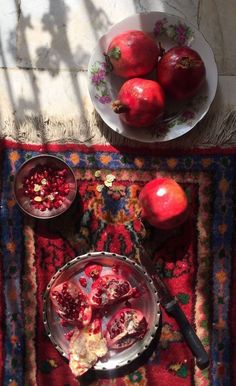 pomegranates are in bowls on a rug next to a bowl of fruit