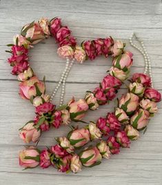 pink flowers arranged in the shape of a heart on a white wooden background with pearls