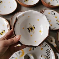 a person holding a plate with yellow flowers and bees on it next to other plates