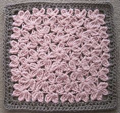 a crocheted square with pink and gray flowers on the center is sitting on a carpet