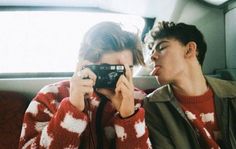 two people sitting in the back seat of a car, one taking a photo with a camera