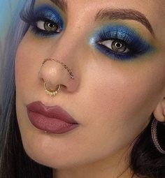 a woman with blue and yellow makeup is wearing a nose ring, piercings on her nose