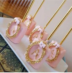 pink and gold cake pops with numbers on them sitting on a white plate next to golden forks