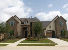 a large brick house with two garages and trees in the front yard on a cloudy day