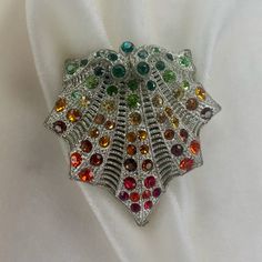 A very special vintage restored unsigned rhinestone clip with multicolored rhinestones.  The clip came in a lot of discarded jewelry.  It is about 2" x 2". The clip is old; it appears to be made of silver tone base metal. The clip is unsigned. Because so many stones were missing or in poor condition, I found vintage stones in fall colors and had a bit of fun with the restoration. The clip mechanism is in excellent working order. The clip can now be worn instead of getting thrown away. A beautiful dramatic piece! Collectible Multicolor Costume Jewelry Brooches, Vintage Multicolor Multi-stone Brooch, Crystal Rhinestone Brooches For Costume Jewelry, Crystal Rhinestone Brooches Costume Jewelry, Multicolor Brooch Jewelry For Evening, Multicolor Brooch For Evening Wear, Vintage Multicolor Wedding Brooches, Multicolor Costume Jewelry Brooches For Weddings, Elegant Multicolor Collectible Brooches