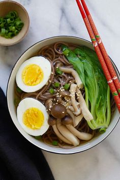 a bowl filled with noodles and vegetables next to chopsticks on a marble surface