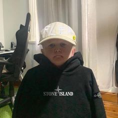 a young boy wearing a black hoodie and a white hat with the stone island logo on it