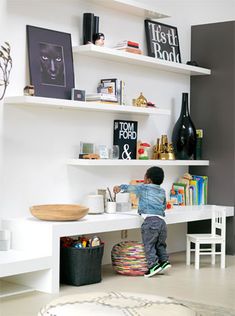 a little boy standing on top of a white desk next to a shelf filled with books