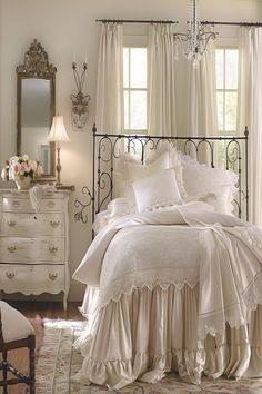 a bedroom with white bedding and chandelier hanging from the ceiling next to a window