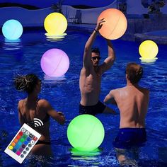 three men and two women playing with balls in a pool at night time, while one man watches from the sidelines