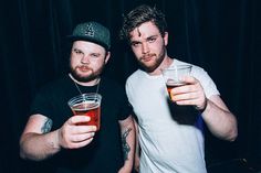 two men standing next to each other holding drinks