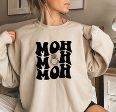 a woman wearing a sweatshirt with the words mom on it and a ring in her hand